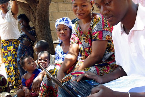 Man on a laptop while two women look over his shoulder