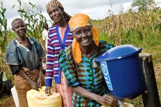 Three woman treating their water with chlorine with a dispenser from Evidence Action.