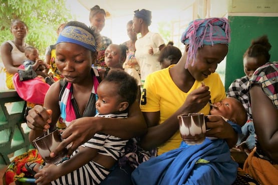 Two women spoon-feeding their babies in a group