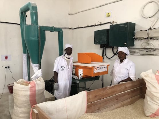 Two small-scale mill workers standing next to a Sanku dosifier