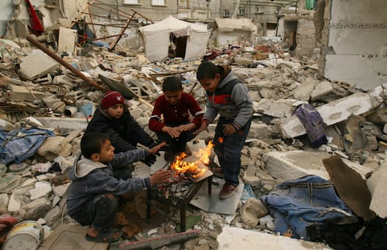 Four boys huddled around fire in rubble in Gaza