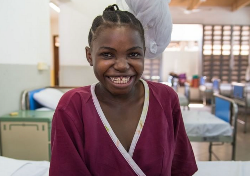 A young fistula patient smiling and sitting on a Fistula Foundation hospital cot