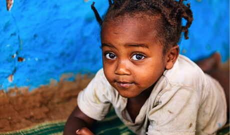 A young Black girl with wide eyes kneeling in front of a blue wall