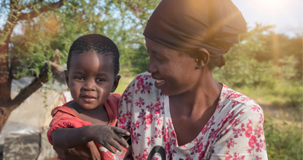 Woman in white and pink flower top holding her child in rural Africa