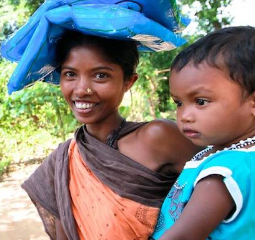 A woman carrying a stack of bednets on her head, a child on her hip